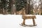 A roughly made wooden children`s rocking - a horse in a clearing against a background of white snow and trees in a city park