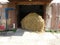 Round bale of hay lies in the opening of the open gate of the stable on a summer day