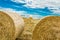 Round bales of hay on farmland with blue cloudy sky