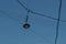 Round black pendant glass lamp hanging from crossing wires above city road in blue sky in light