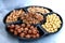 A round black serving platter with five compartments full of assorted shelled nuts hazelnuts, cashews, peanuts, walnuts