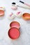 Round blusher pots with different shades of pink and cute powder puffs with ribbons and makeup brushes