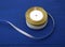 Round bobbin with silver and golden ribbon on a blue wooden background