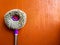 Round broom cloth mop rotary violet handle leaned on orange wall as background with space for text