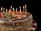 Round cake with candles, on a black background. A sweet birthday present for a teenager. A festive dessert for the whole family