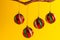 Round colored Christmas ornaments hanging from golden branch against yellow background