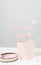 Round craft pink present box and sweet pink hearts in it on the white surface against grey wall.Vertical shot.Concept of valenite`