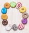 Round frame of colorful doughnuts on white wooden background, top view