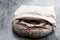 Round freshly baked rye bread in paper bag on gray background