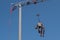 A round grey concrete mixer and a red movable carriage trolley are suspended from the boom hook of a tower crane