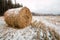 Round hay bale covered by snow left on a field in late autumn