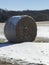 Round hay bale sitting in a farm field on a sunny day in winter after harvest