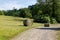 Round hay bales freshly harvested on a gray gravel path in front of a mowed meadow, in the background green summer forest with