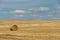 A round haystack in a field against a background of blue sky and fluffy clouds. The season of harvesting and grain crops.