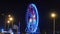 A round large Ferris wheel with multicolored illumination lights, an attraction in city park at night