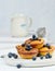 Round mini cottage cheese pies with blueberries on a white wooden board, delicious sweet dessert