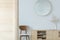 Round mirror above wooden chair and cabinet in minimal anteroom interior with decor