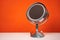 Round mirror on metal stand with backlight stands on table on orange background, copy space for text, front view.