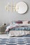 Round mirror in wooden frame above king size bed with blue, beige and pastel pink bedding