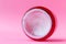 Round open red plastic jar with with white cream inside on a pink background with copy space. Skin care, cosmetics concept. Beauty