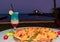 Round pizza on wooden board and Blue Hawaii cocktail on restaurant table by the lake