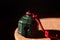 On a round plate made of cork stands a green metal bell, with a red cord on it, against a dark background