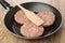 Round raw cutlets and spatula in frying pan on table