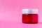 Round red plastic jar with a white cap on a pink background with copy space. Skin care, cream, cosmetics concept. Beauty packaging