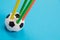 A round soccer ball shape pencil cup with five colorful pencils in it on azure surface isolated