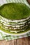 Round spinach crepes cake with cheese cream close-up on a plate.