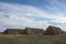 Round stacks of dry yellow hay lie in rows of pyramids in a meadow under a blue sky