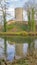 Round tower of castle ruins on a hill, bare trees, moat with the tower reflected in the water surface