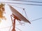 Round tv antenna against the sky. A rusting white satellite dish on a peeling pole among the wires against the sky