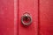 A round and twisted cast iron door knocker fitted on an old wooden door painted in red