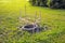 A round, uncovered sewer pit is fenced off for safety with warning tape on wooden posts