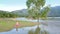 Round view lady sits on mat tree reflects in lake water