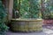 Round water well with faucet in a cemetery with old trees