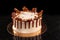 Round white cake with caramel and chocolate puffed rice on a round tray on black background