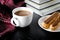 A round white cup and saucer stands on a white wooden table next to books and yellow autumn leaves