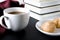 A round white cup and saucer stands on a white wooden table next to books and yellow autumn leaves