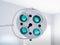 Round white swivel medical operating lamp with four green blue turquoise lights in doctor`s office. White interier,