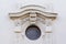 Round window on a white stone wall decorated with ornate stucco