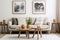 Round wooden coffee table near beige sofas against white wall with posters. Scandinavian style home interior design