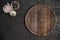Round wooden cutting board on black table. Top view of empty kitchen trendy rustic wooden tray.