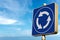 Roundabout Road Sign against a Clear Blue sky with Clouds - Photography