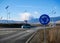 Roundabout traffic sign, passing cars in the background, solar panels providing the light at night.