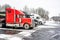 Row of big rigs industrial semi trucks with semi trailers standing on the winter truck stop parking lot with snow and ice