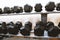 A row of black metal dumbbells of different weights on a rack in the gym