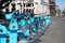 A row of blue rental bicycles sits along a city street