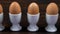 Row of boiled eggs in egg cups on a wooden table to toast soldier being dipped in the yolk of a broken open egg